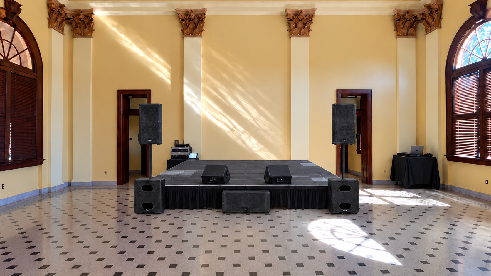 Illustrative Pink Friday venue setup with stage, left and right speaker stacks, center subwoofer, two stage monitors, a control rack at audience left and DJ station offstage right.